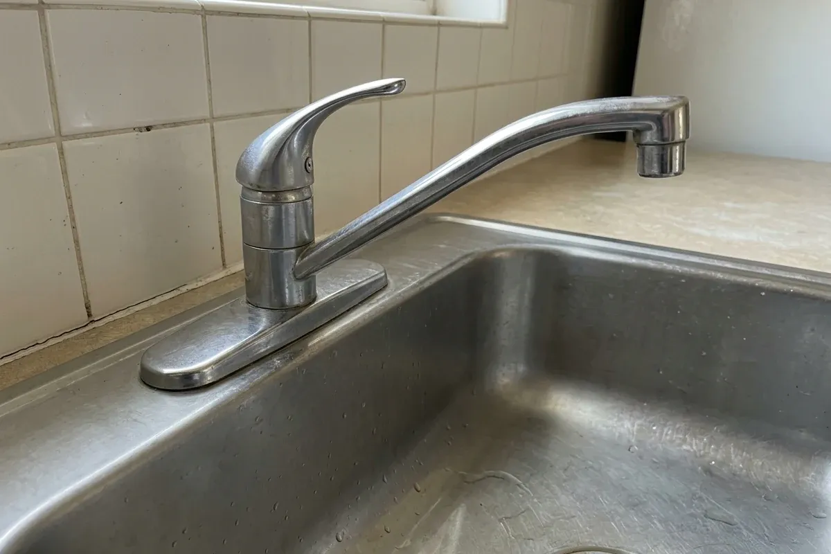Existing faucet base mounted through a sink deck with the surrounding deck visible