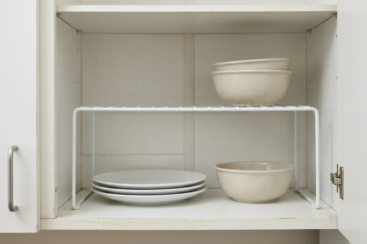 Loose shelf riser resting inside an existing kitchen cabinet with dishes above and below it